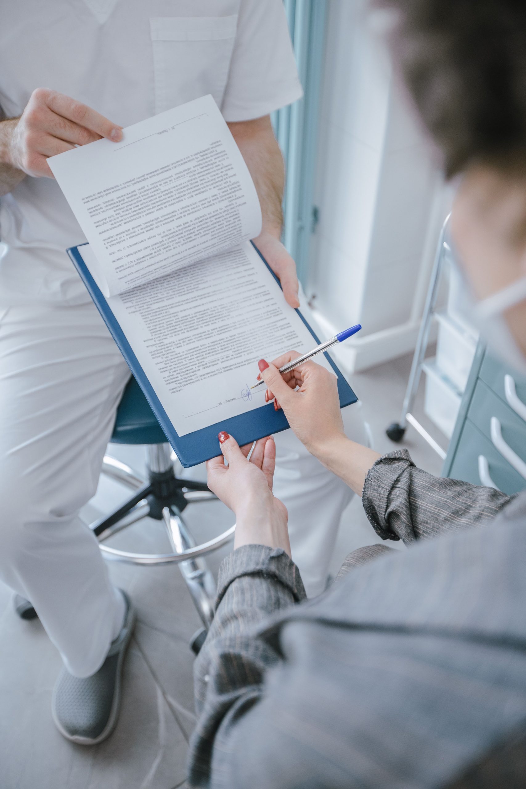 Patient signing a document on a clipboard held by a healthcare professional during a medical appointment